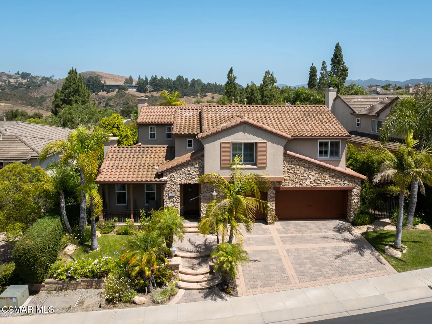 Two-story suburban home with stone facade, tile roof, attached garage, and landscaped front yard with palm trees.