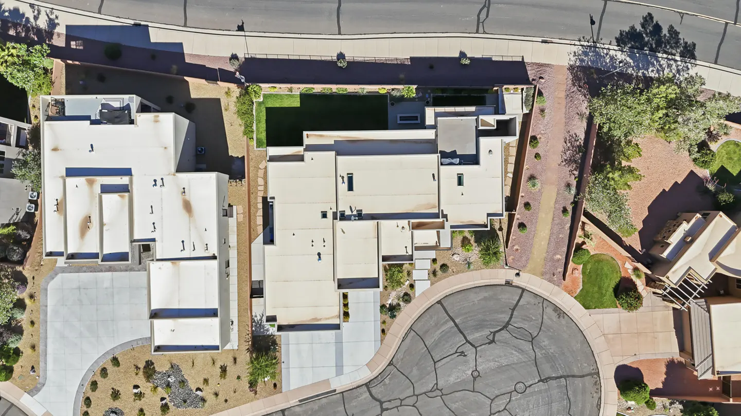 Aerial view of a modern flat-roofed home with a small green lawn, concrete driveway, and desert landscaping in a cul-de-sac.
