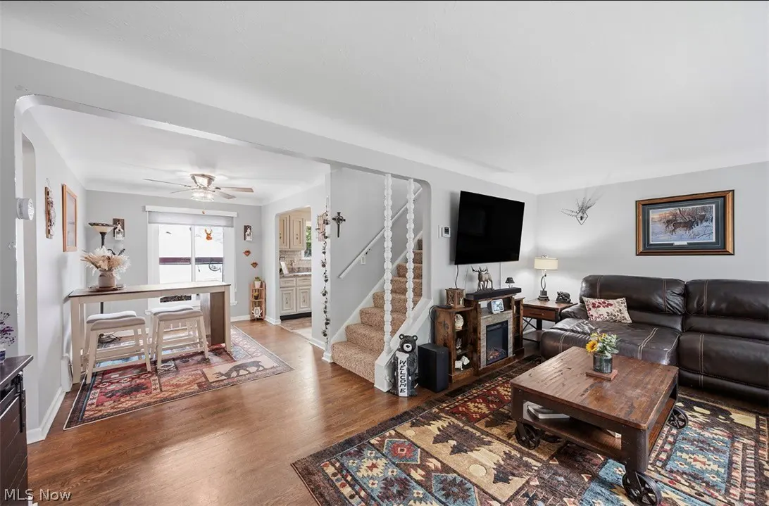 Open-concept living room with hardwood floors, brown leather sofa, and a staircase leading upstairs. A table with stools is visible.