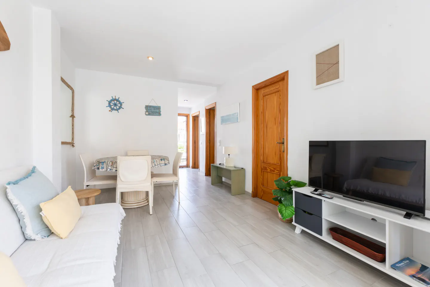 Bright living room with white walls, light wood floors, and nautical decor. A white sofa and dining set are visible.