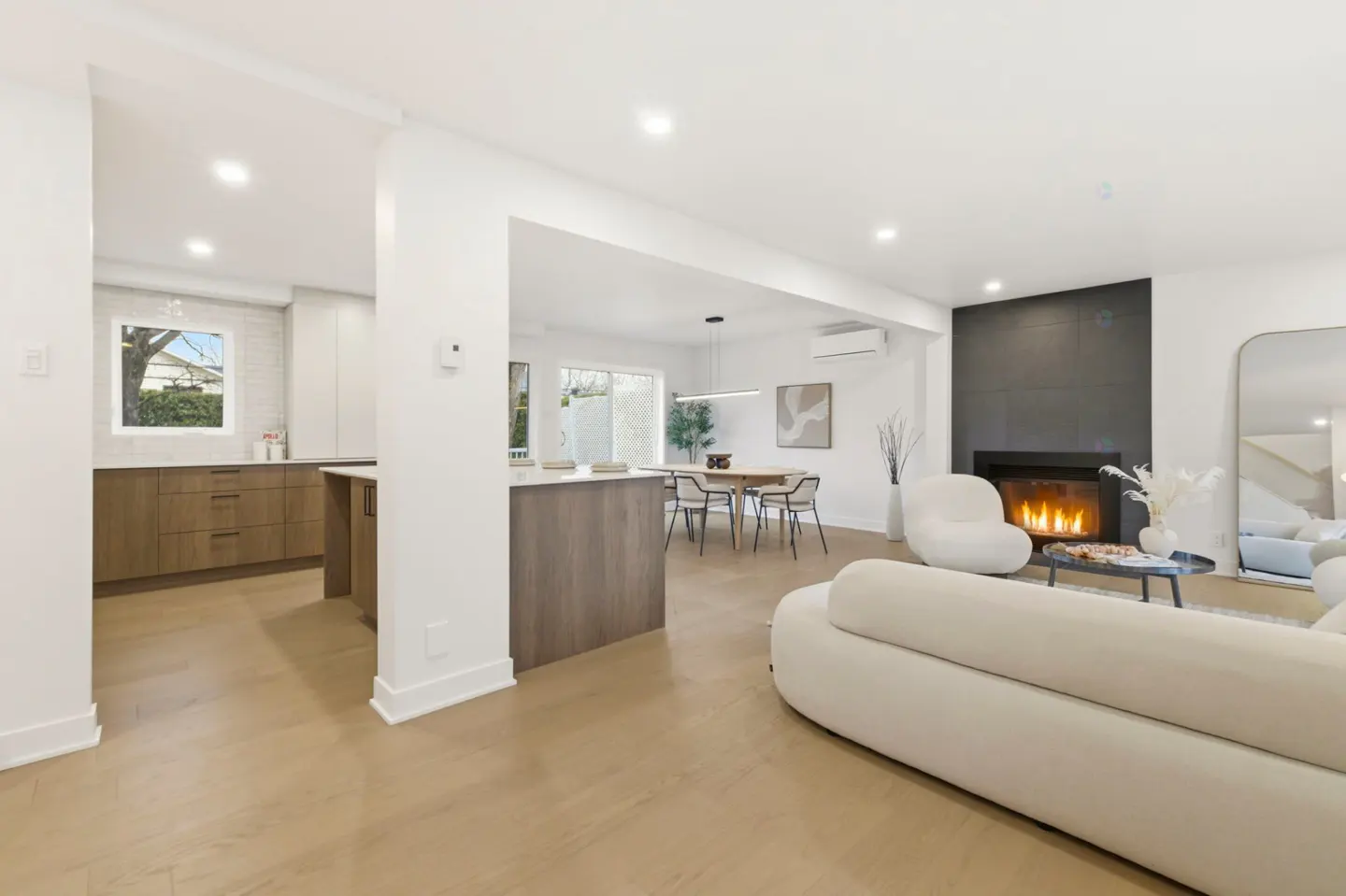 Open-concept living space with a kitchen, dining area, and living room. Features a fireplace, white sofa, and wood floors.