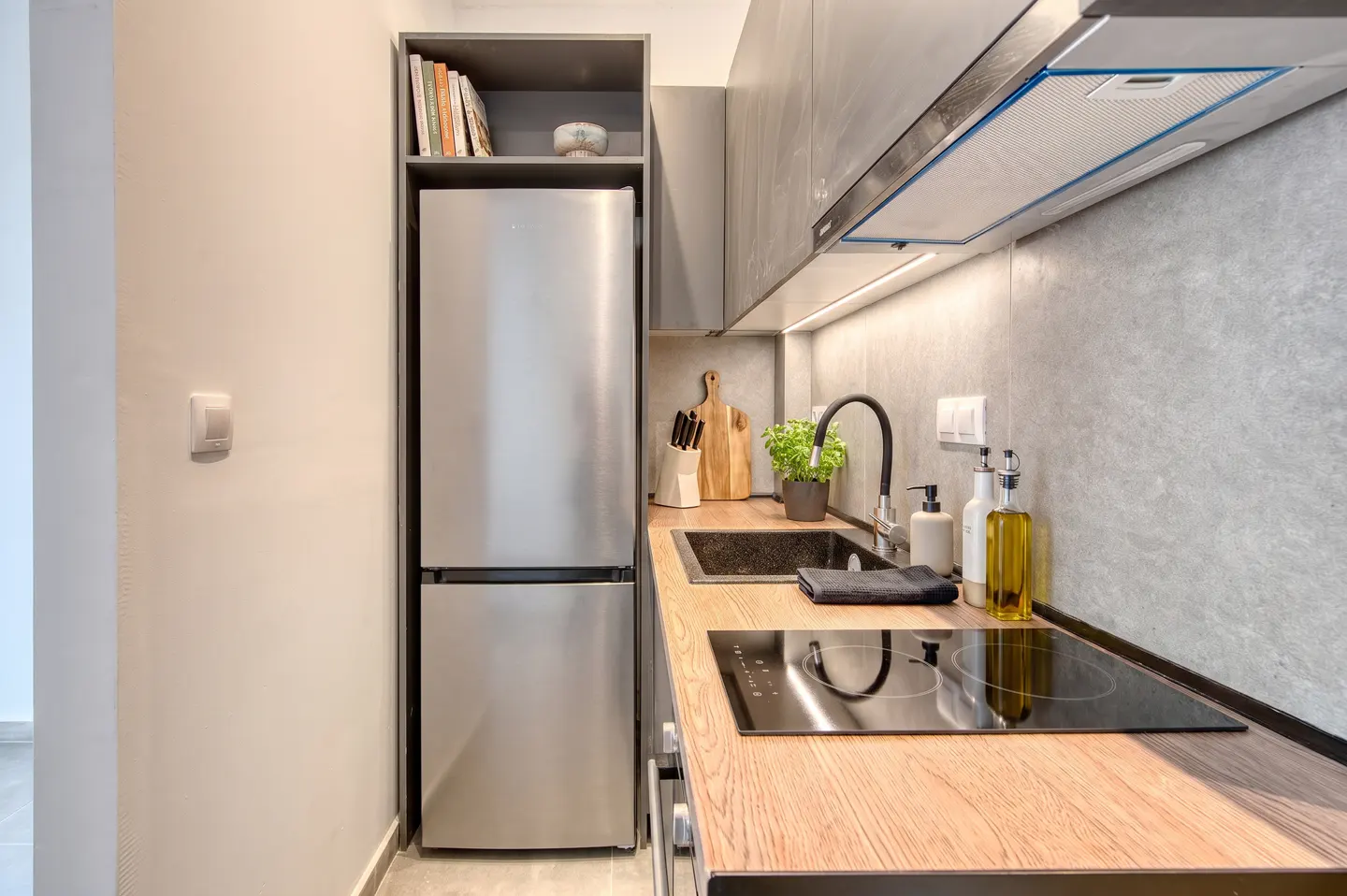 A modern kitchen with stainless steel refrigerator, wood countertop, black sink, and electric cooktop.