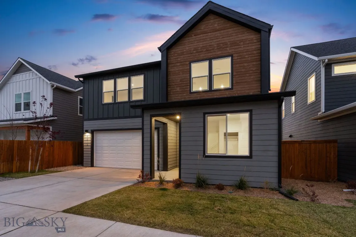 Modern two-story home with gray and wood siding, white garage door, and a concrete driveway at dusk.