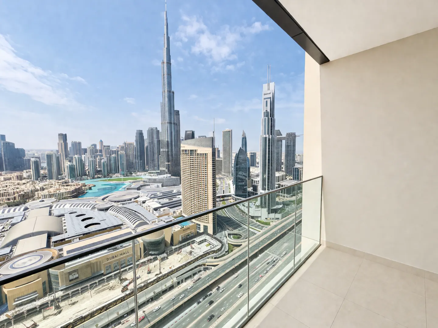 View from a balcony overlooking the Dubai skyline, including the Burj Khalifa and Dubai Mall, with busy roads below.