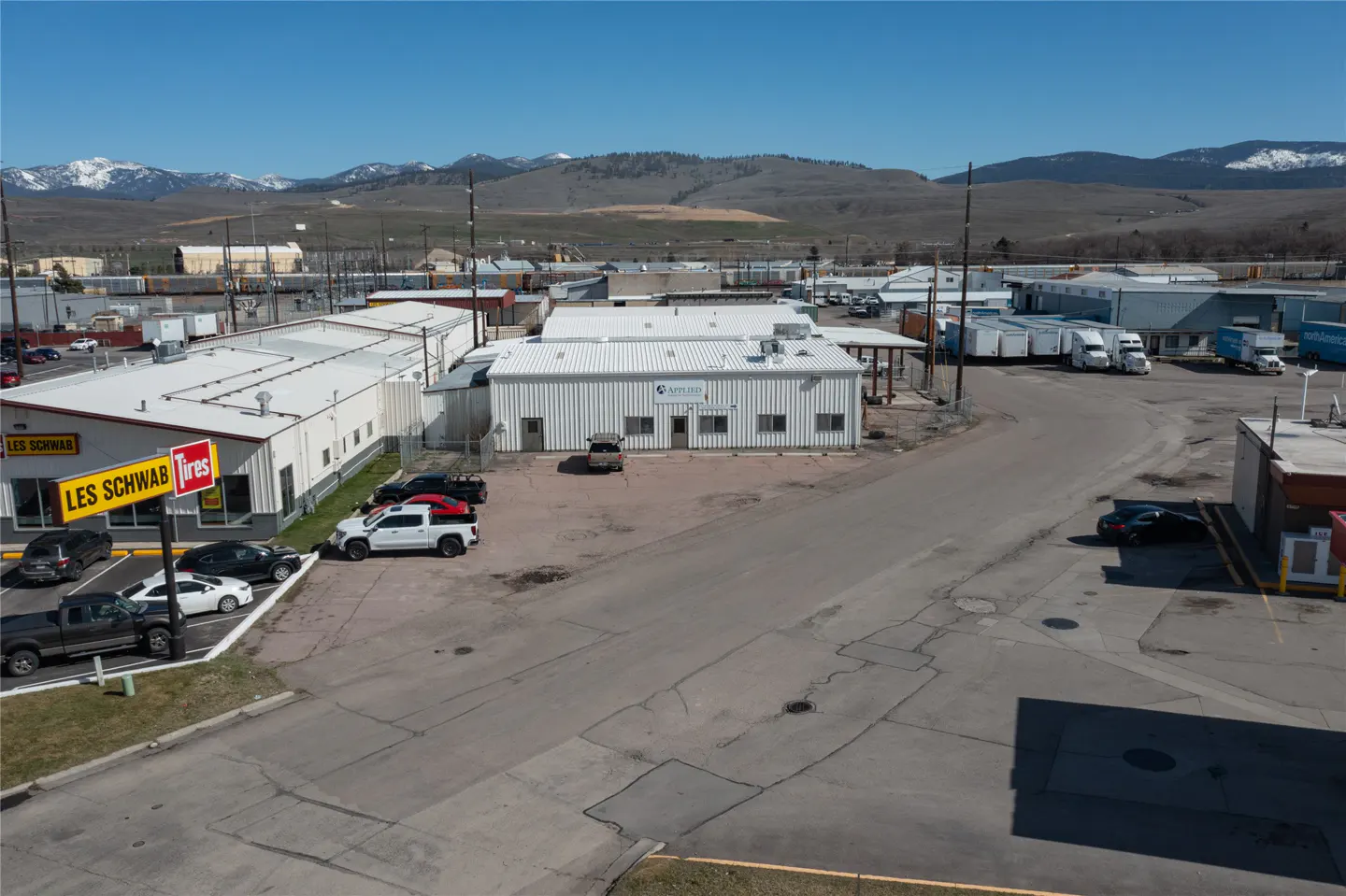 Aerial view of commercial buildings, including Les Schwab Tires, with mountains in the background on a sunny day.