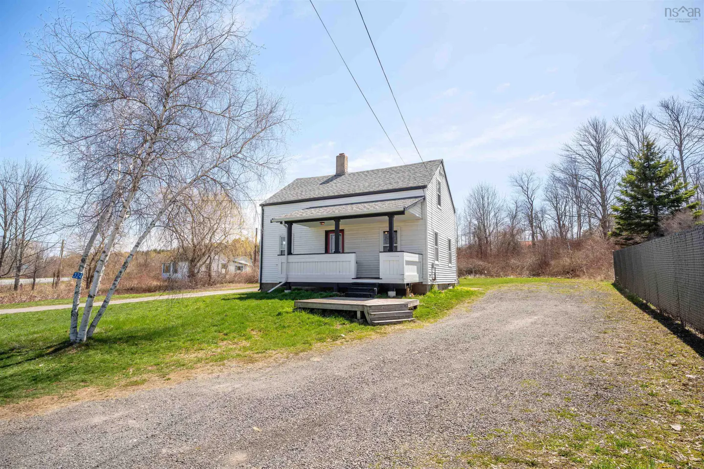 Exterior view of a white, two-story house with a gray roof, a small porch, and a gravel driveway.