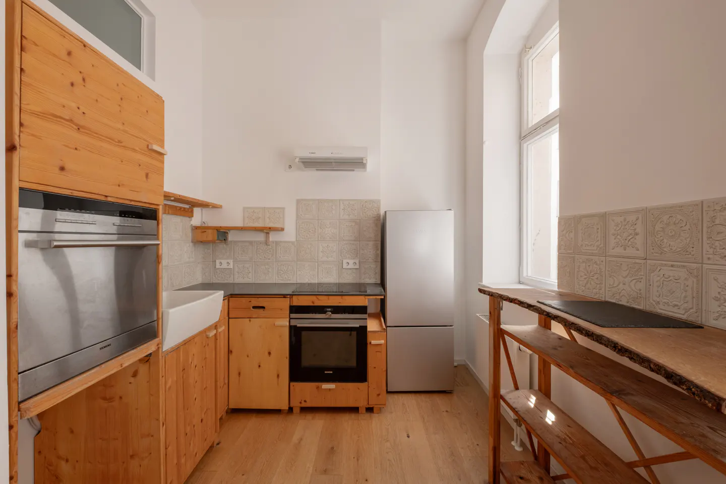 Kitchen with light wood cabinets, stainless steel appliances, patterned tile backsplash, and a rustic wooden shelving unit.