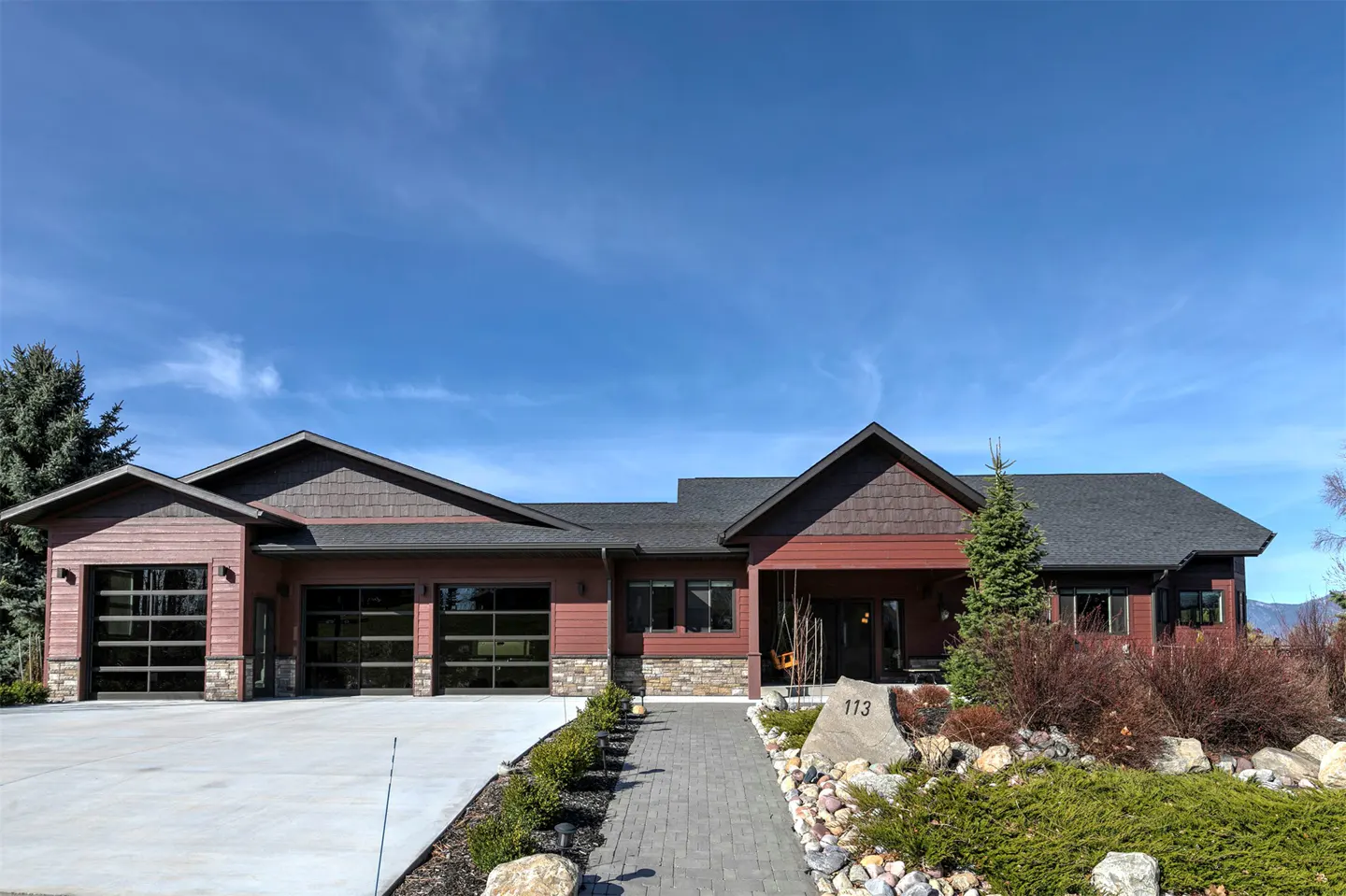 Exterior of a one-story red house with a gray roof, glass garage doors, and a stone walkway leading to the front door.