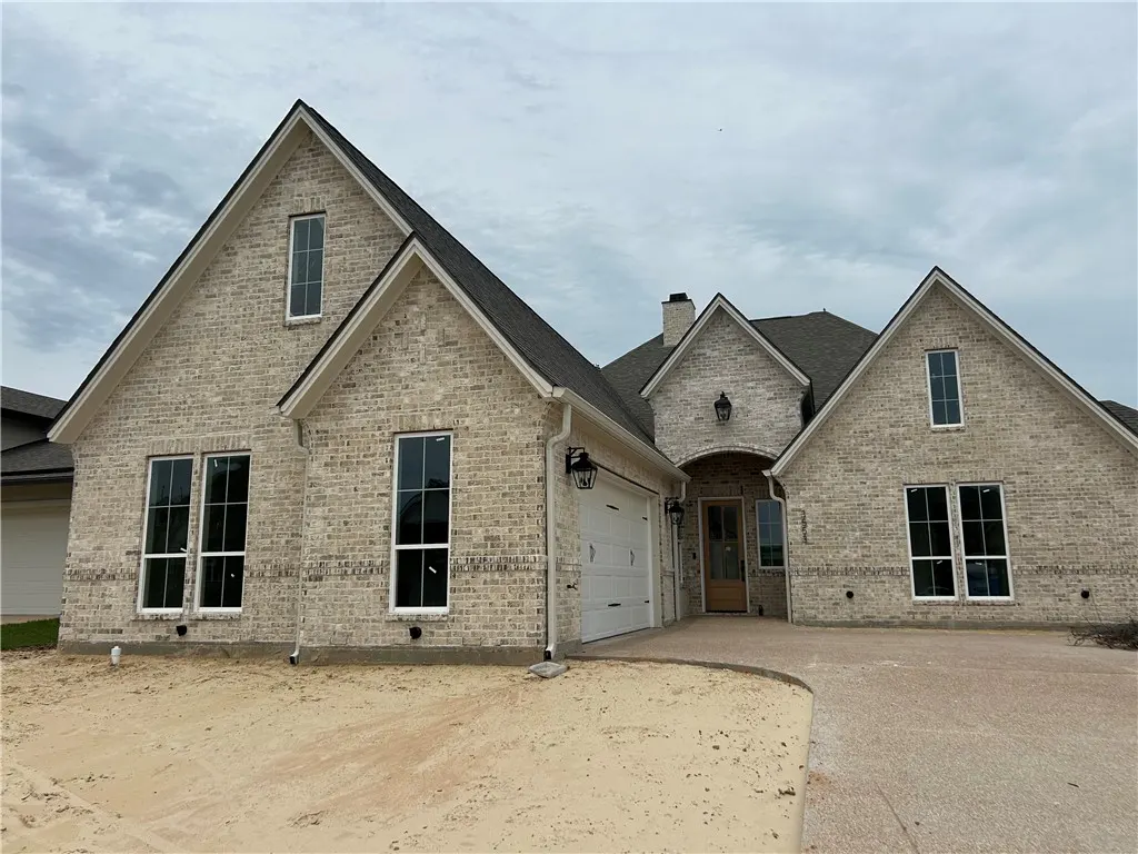 A single-story house with light brick, a gray roof, black-framed windows, and a white garage door. The yard is dirt.