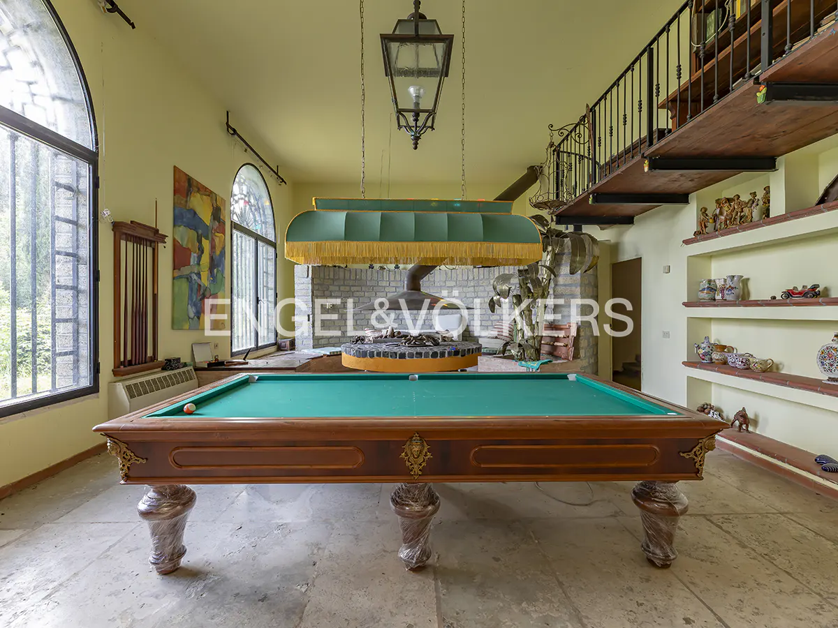 A game room with a green pool table, a fireplace, and a balcony with shelves.