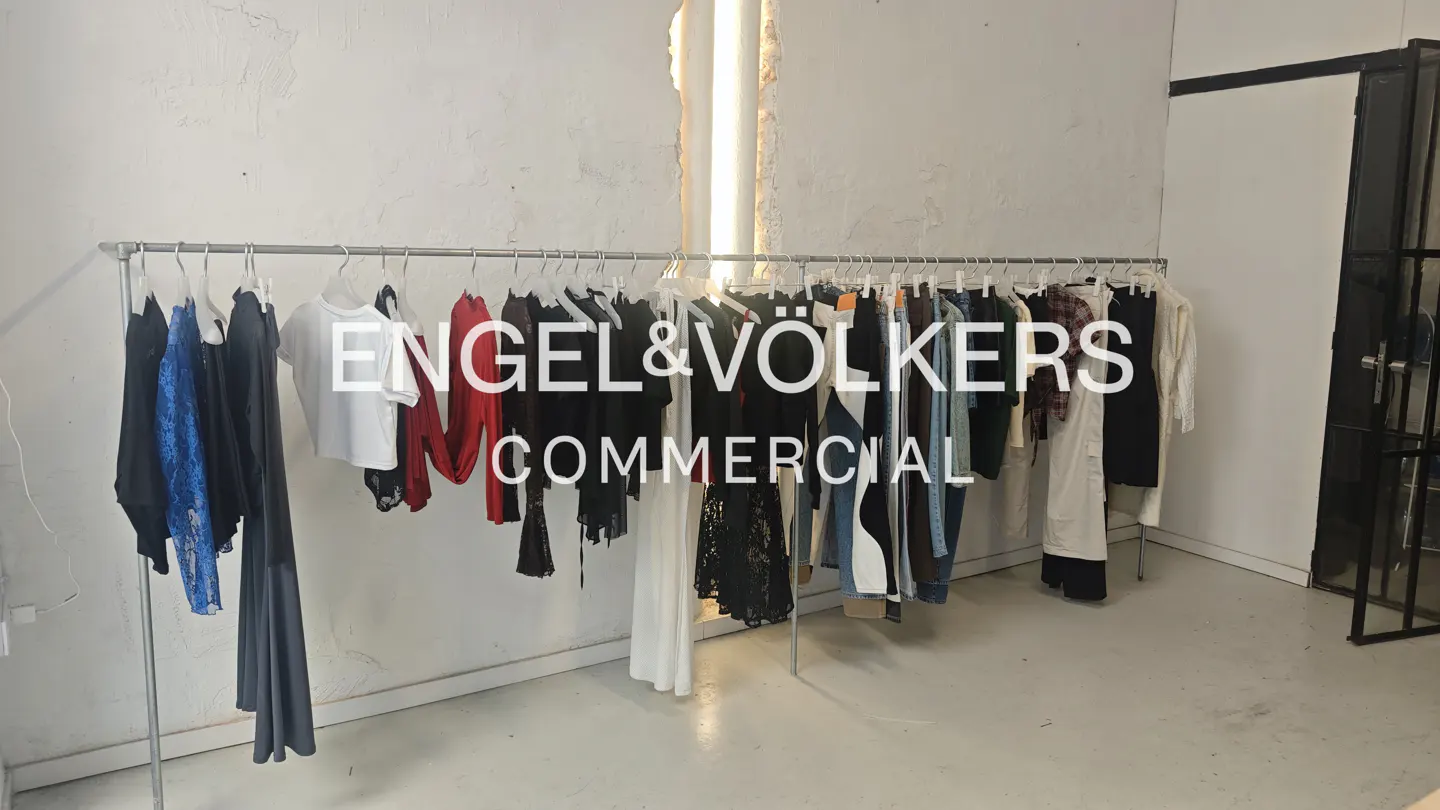 Clothes hang on a metal rack in a bright room with white walls and a concrete floor.