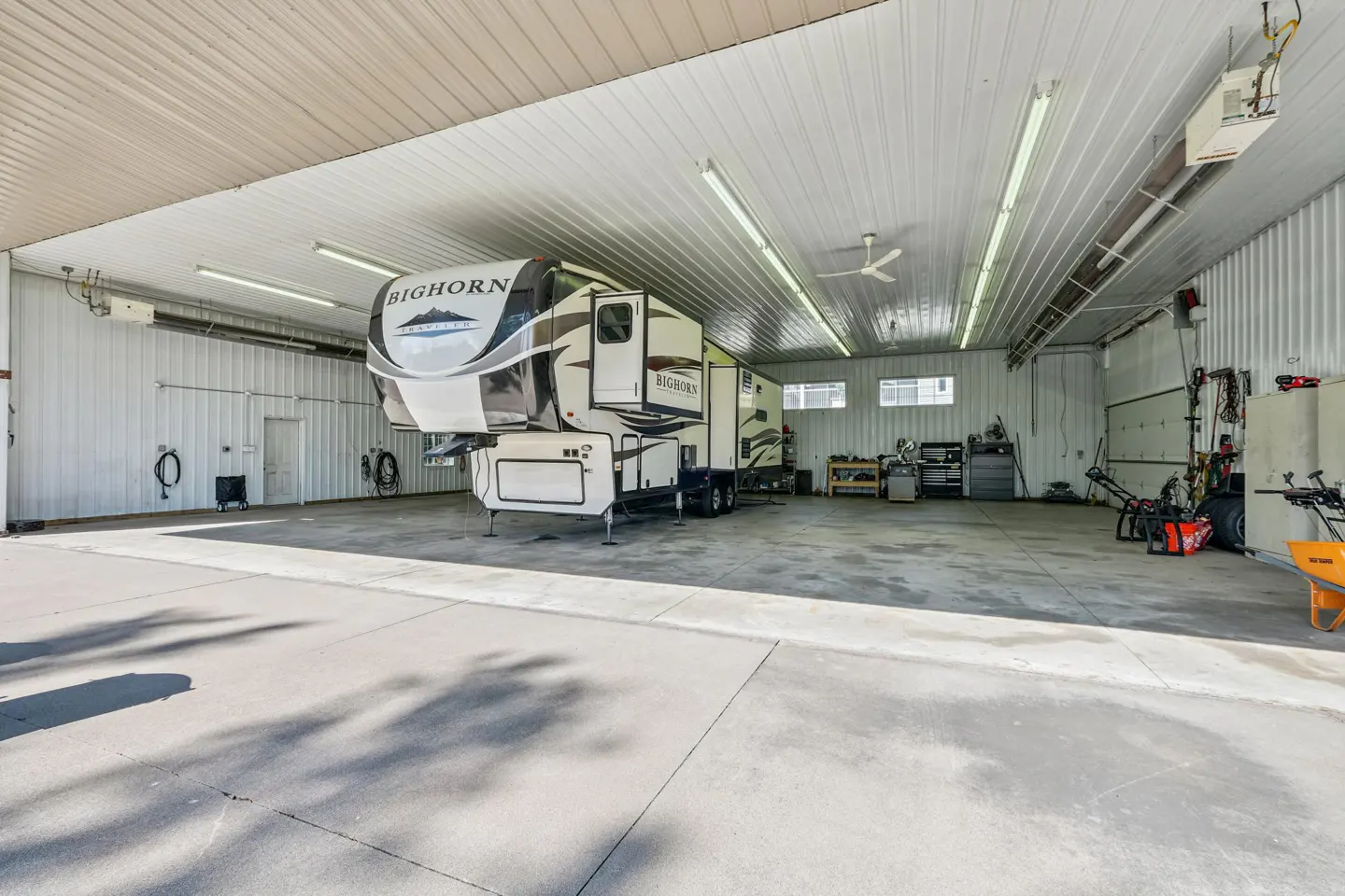 A white and brown Bighorn RV parked inside a large, well-lit garage with white walls and a concrete floor.