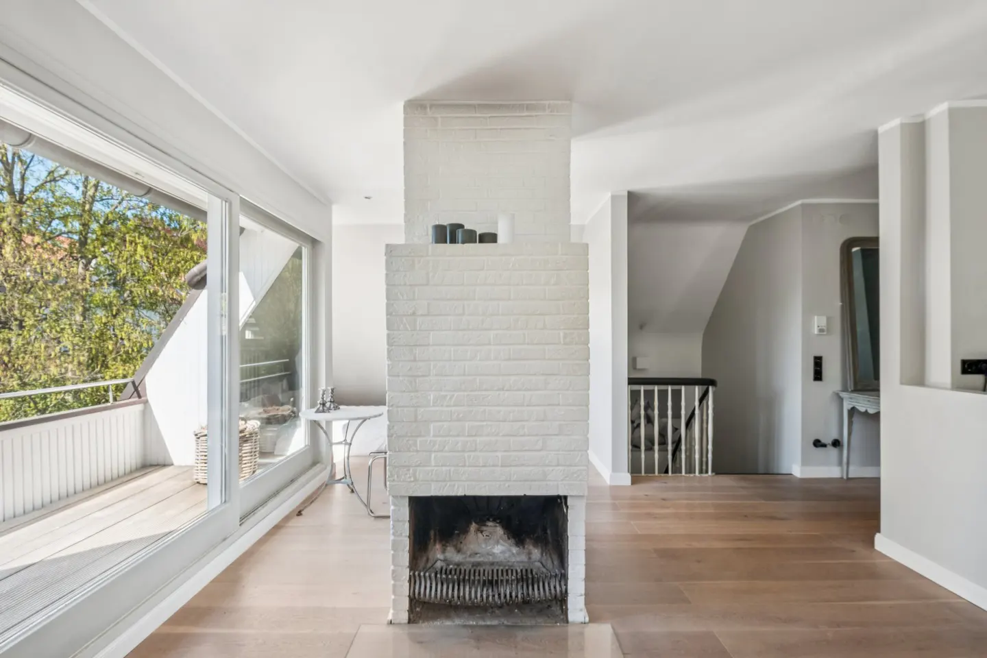 Bright living room with a white brick fireplace, light wood floors, and a balcony with sliding glass doors.