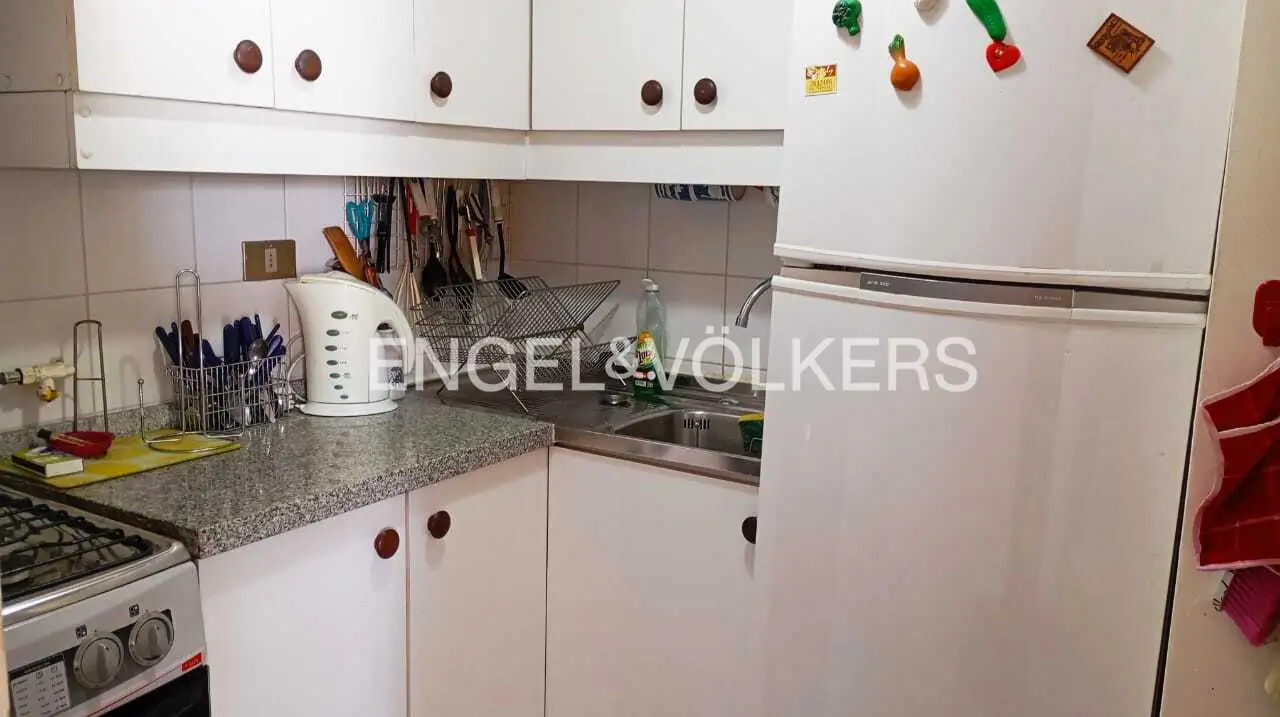 A compact kitchen with white cabinets, a gray countertop, and a white refrigerator. Utensils hang above the sink.