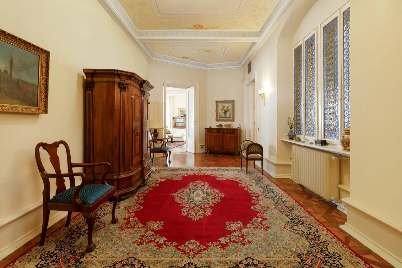 Hallway with a red rug, wooden furniture, and a large window. The ceiling has decorative paintings.