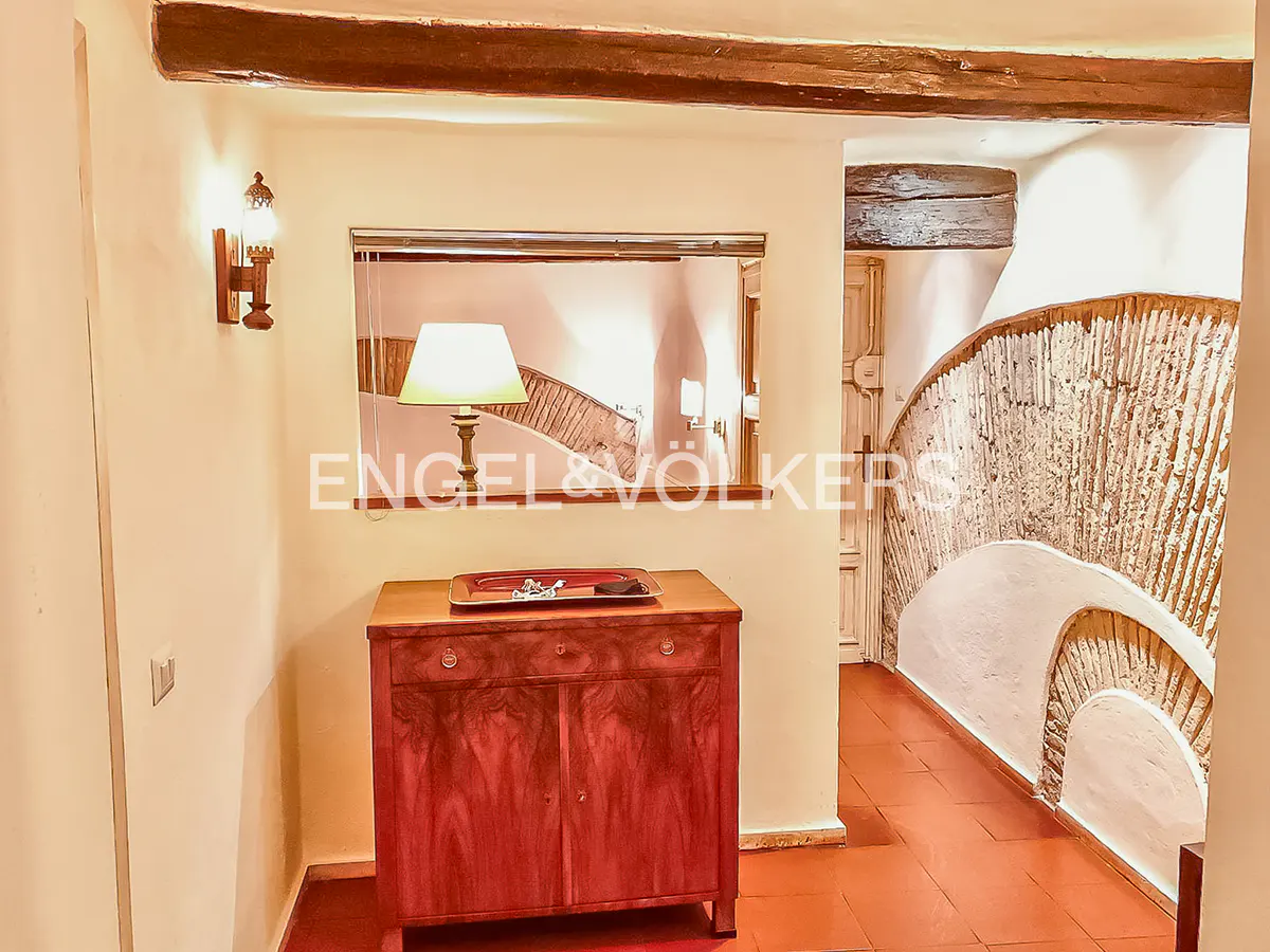 Interior view of a home with a wooden beam ceiling, a red cabinet, and a staircase with a unique textured wall.