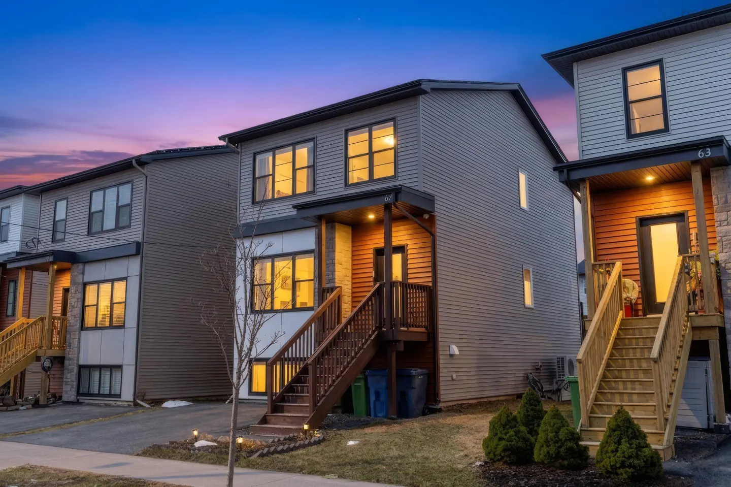 Row of modern two-story townhouses with gray siding and wooden stairs leading to front doors, under a twilight sky.
