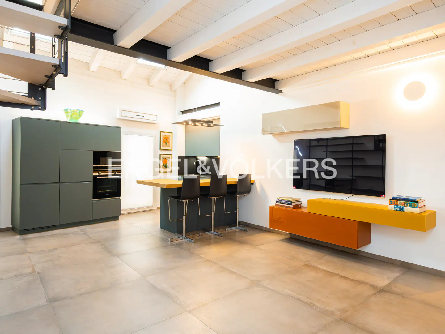 A modern kitchen with gray cabinets, a breakfast bar with black stools, and an orange media console under a flat screen TV.