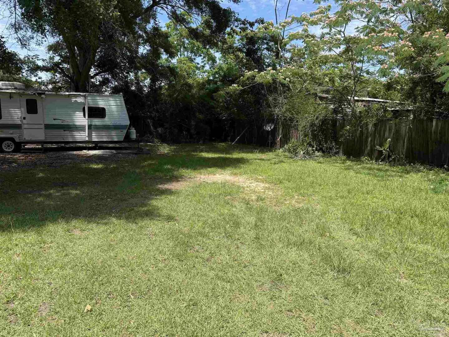 A grassy lot with a camper on the left and a wooden fence in the background.