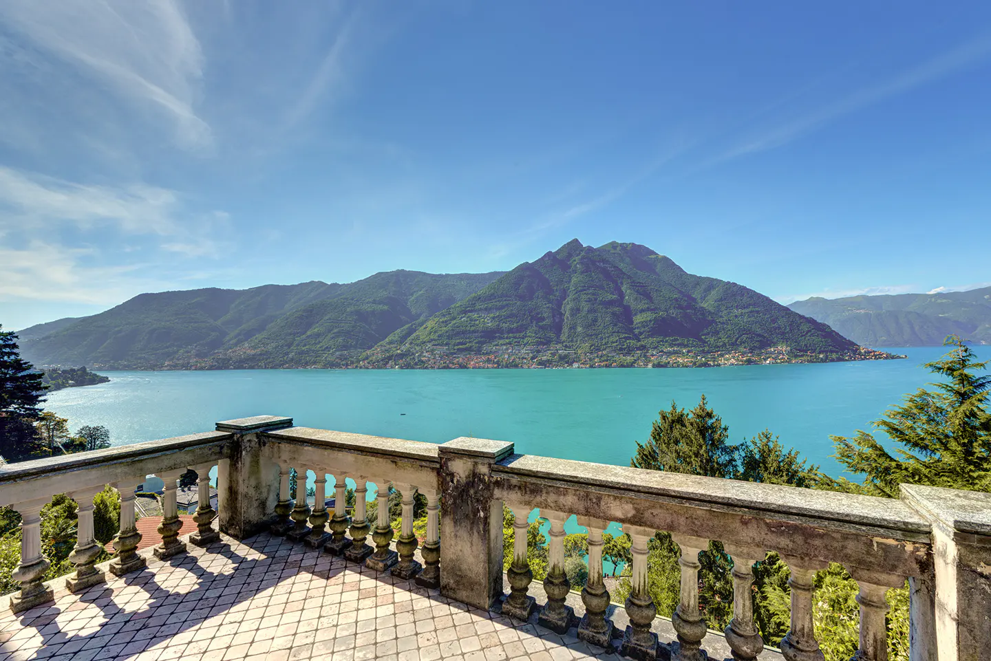 View from a stone balcony overlooking a turquoise lake and green mountains under a blue sky.