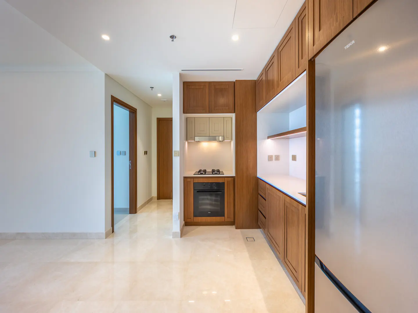A bright kitchen with wood cabinets, stainless steel refrigerator, and marble floors.