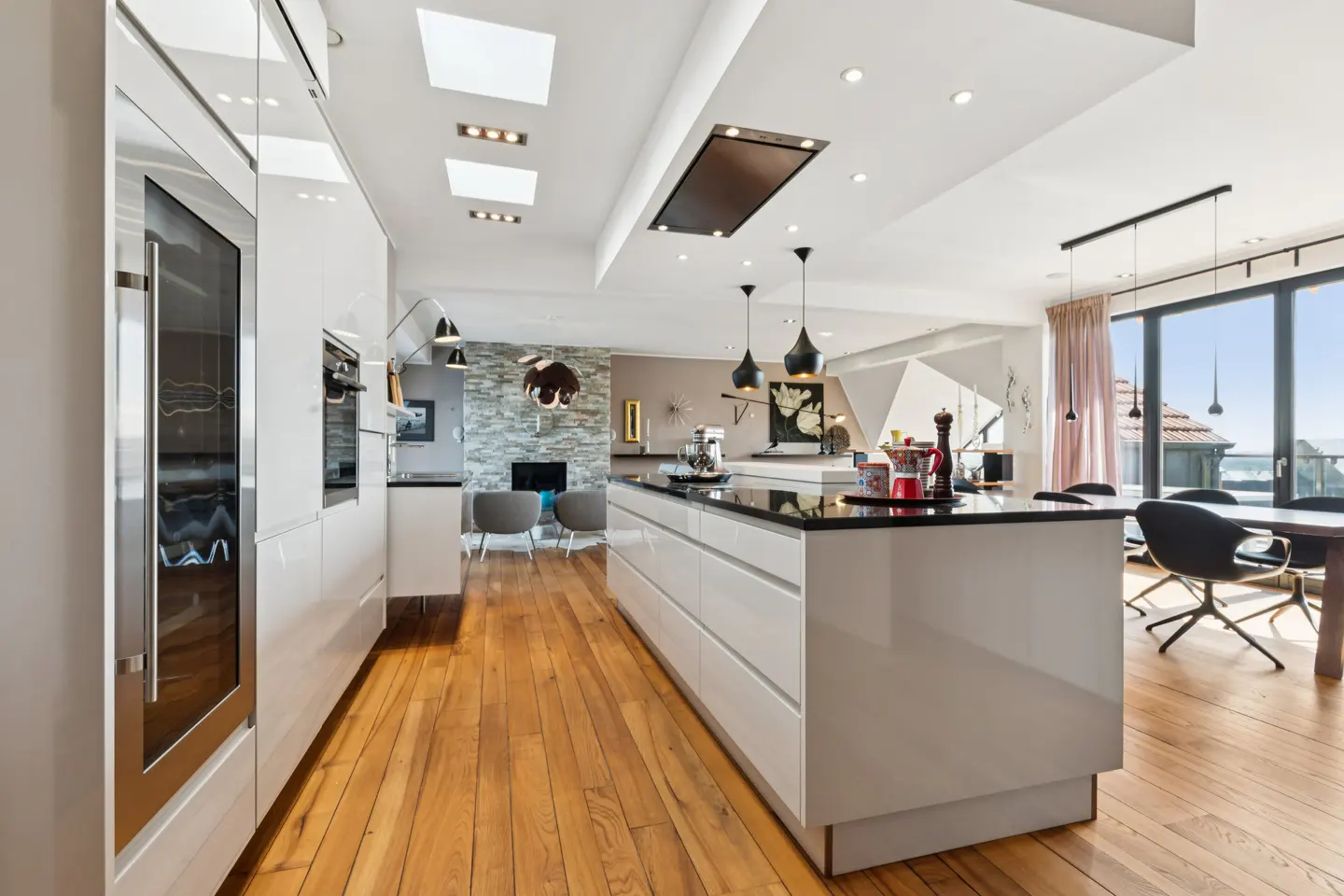 Bright, modern kitchen with white cabinets, black countertops, and wood floors. Skylights and pendant lights illuminate the space.