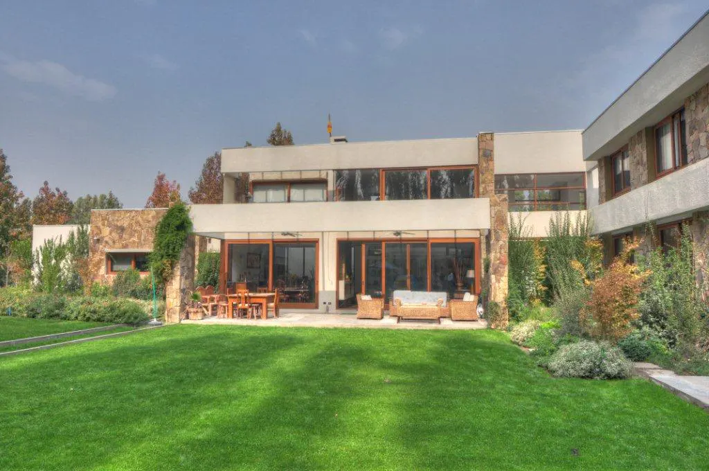 Back view of a modern two-story house with a green lawn, patio furniture, and large windows.