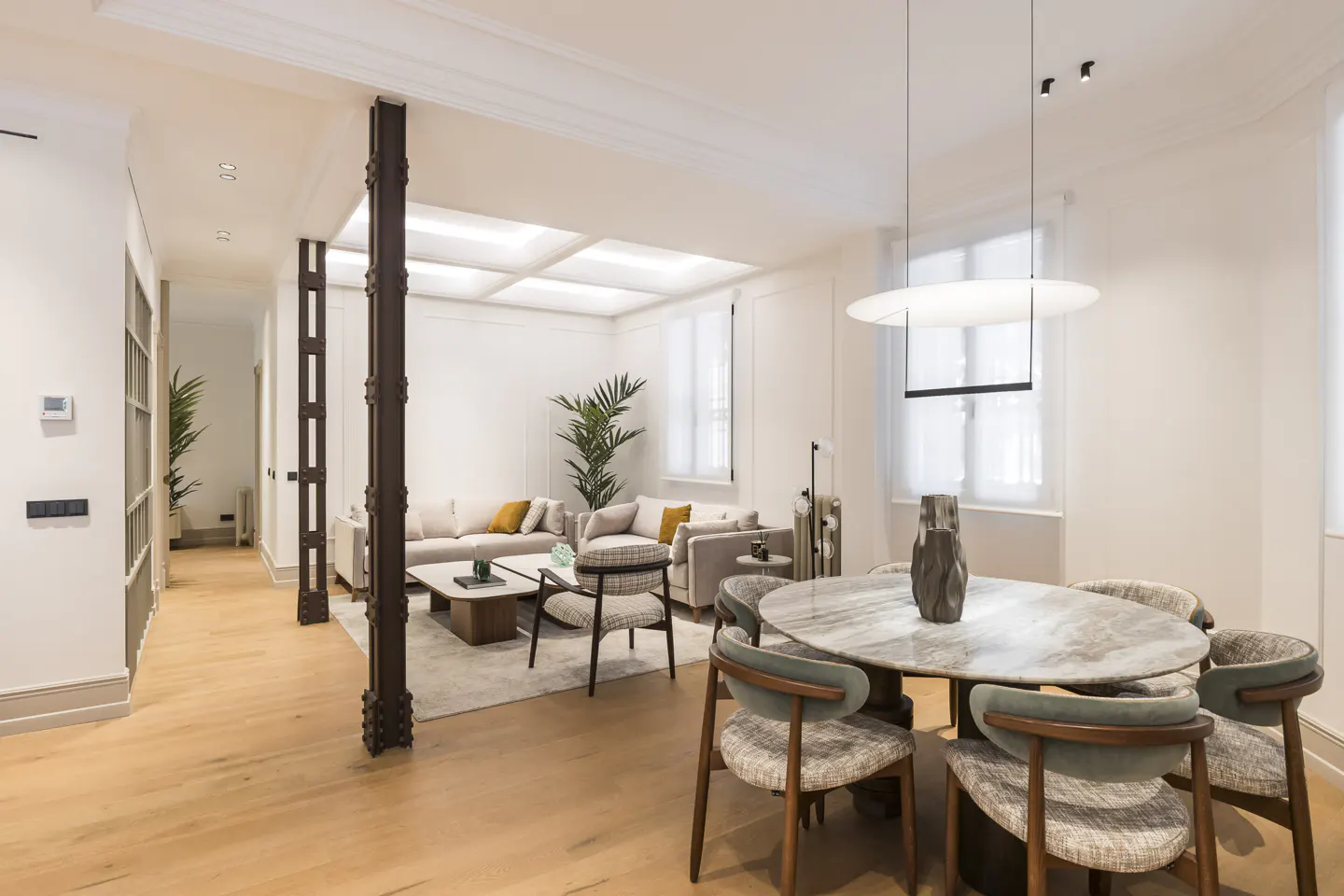 Bright, open-concept living and dining area with hardwood floors. A marble table with six chairs sits near a beige sofa and coffee table.