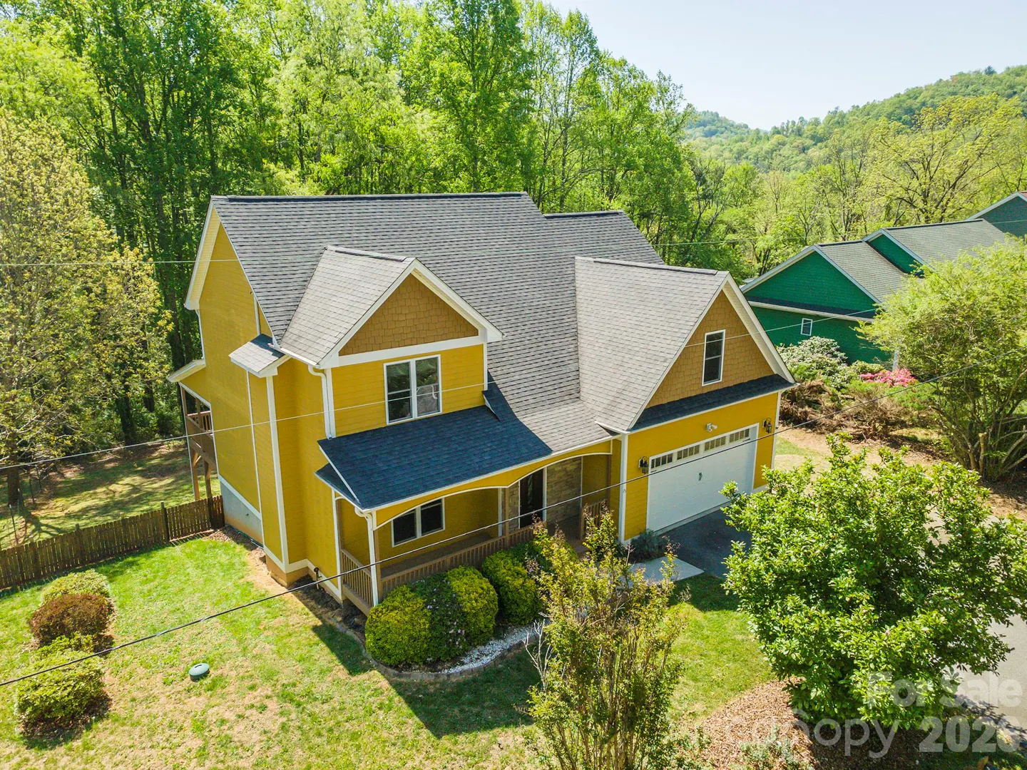Two-story yellow house with a gray roof, a front porch, and an attached garage surrounded by green trees.