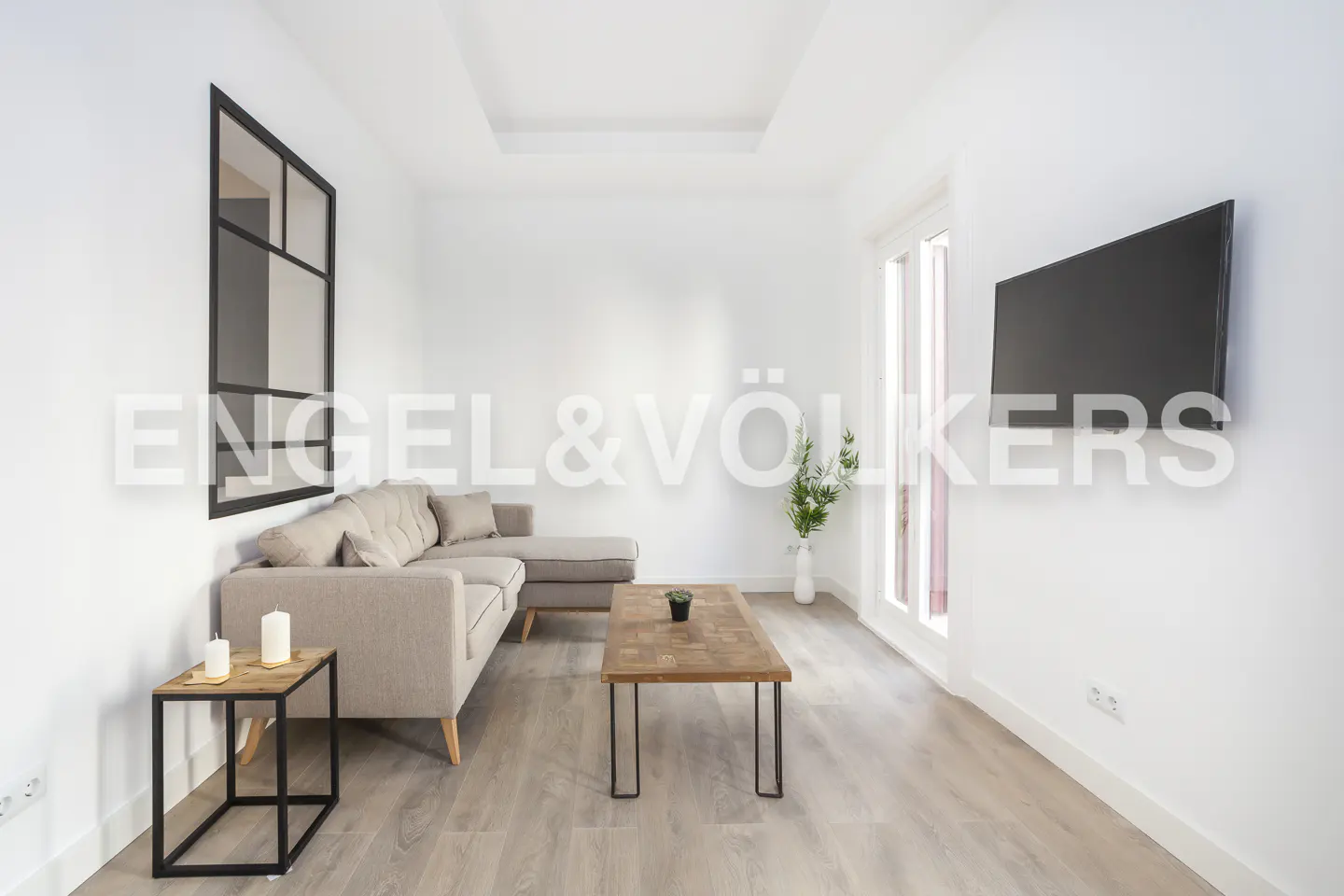 Modern living room with a beige sectional sofa, wooden coffee table, wall-mounted TV, and a large black-framed mirror.