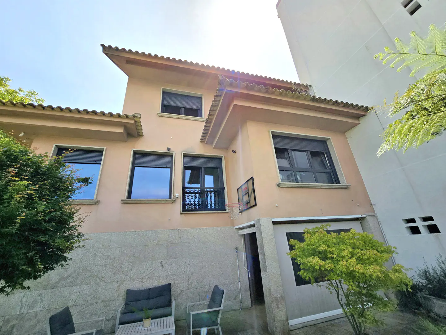 Exterior view of a two-story peach house with a tile roof and dark window shutters. Patio furniture sits on a stone patio.