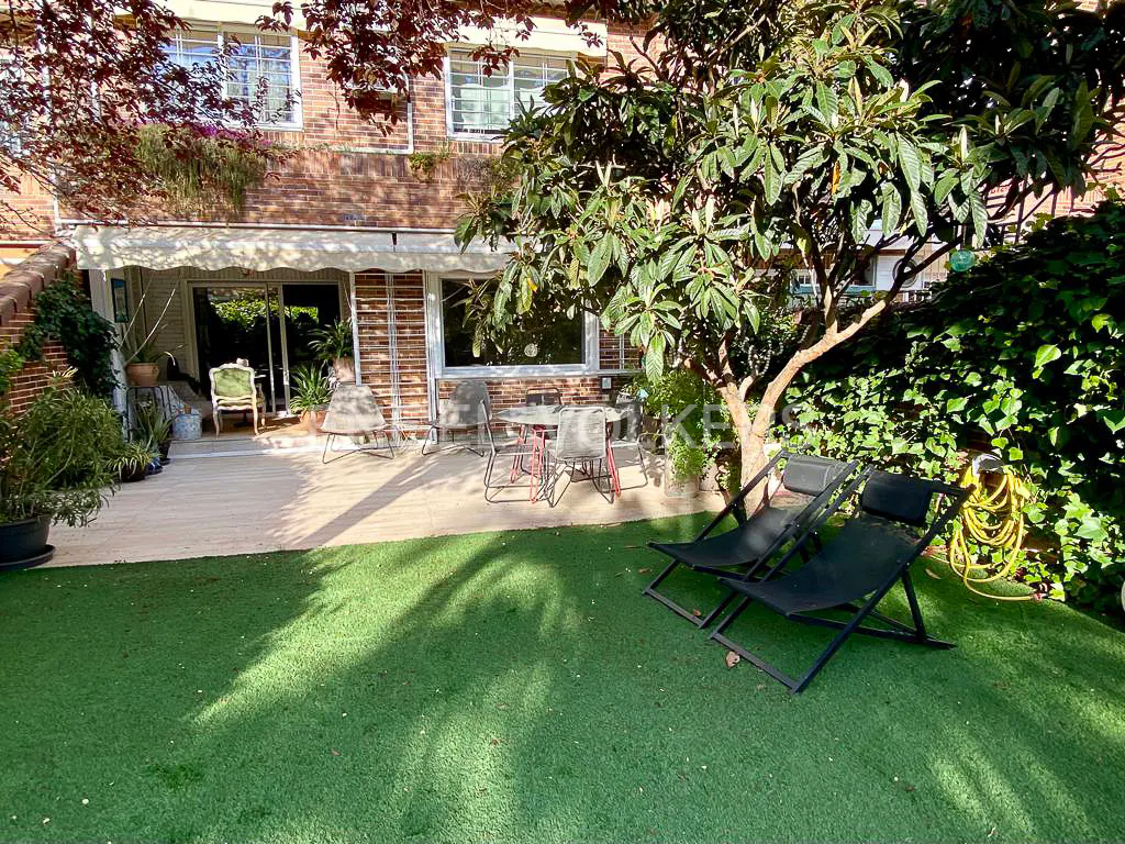 A backyard with a brick house, patio, table, chairs, and two black lounge chairs on green grass.