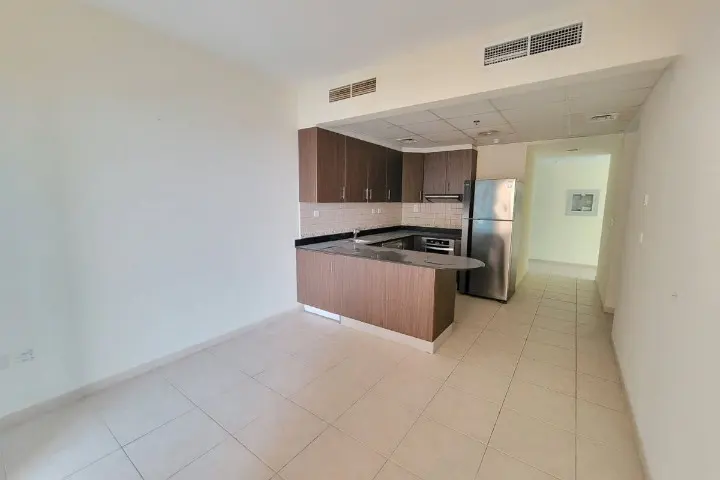 A bright, empty apartment with tile floors, white walls, and a brown kitchen with stainless steel appliances.