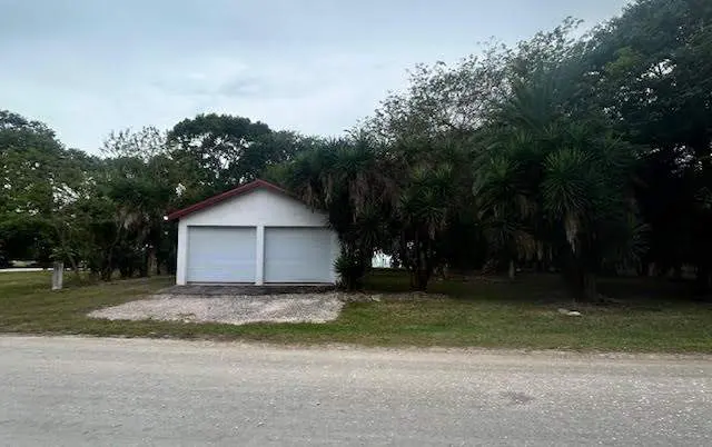 A white two-car garage with a red roof is surrounded by trees and grass.