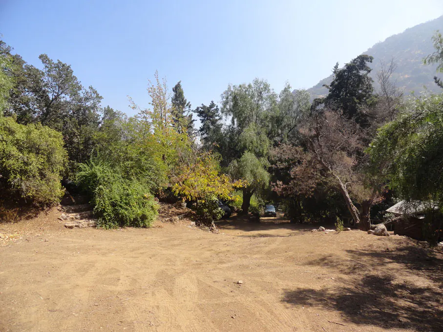 Dirt clearing surrounded by green trees and a mountain under a blue sky.