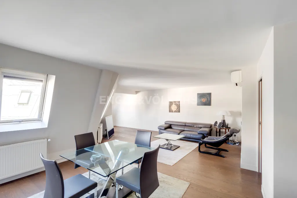 Bright, open-plan living space with a glass dining table, leather sofa, and hardwood floors. Natural light from a dormer window.