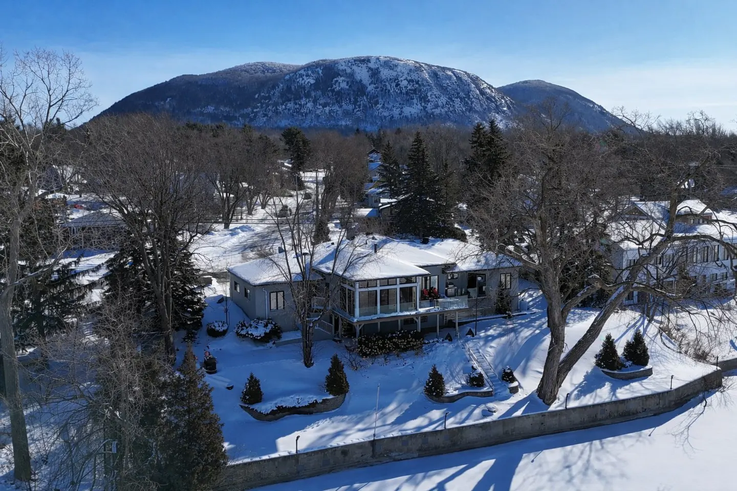 A gray house with a sunroom and a snow-covered mountain in the background.