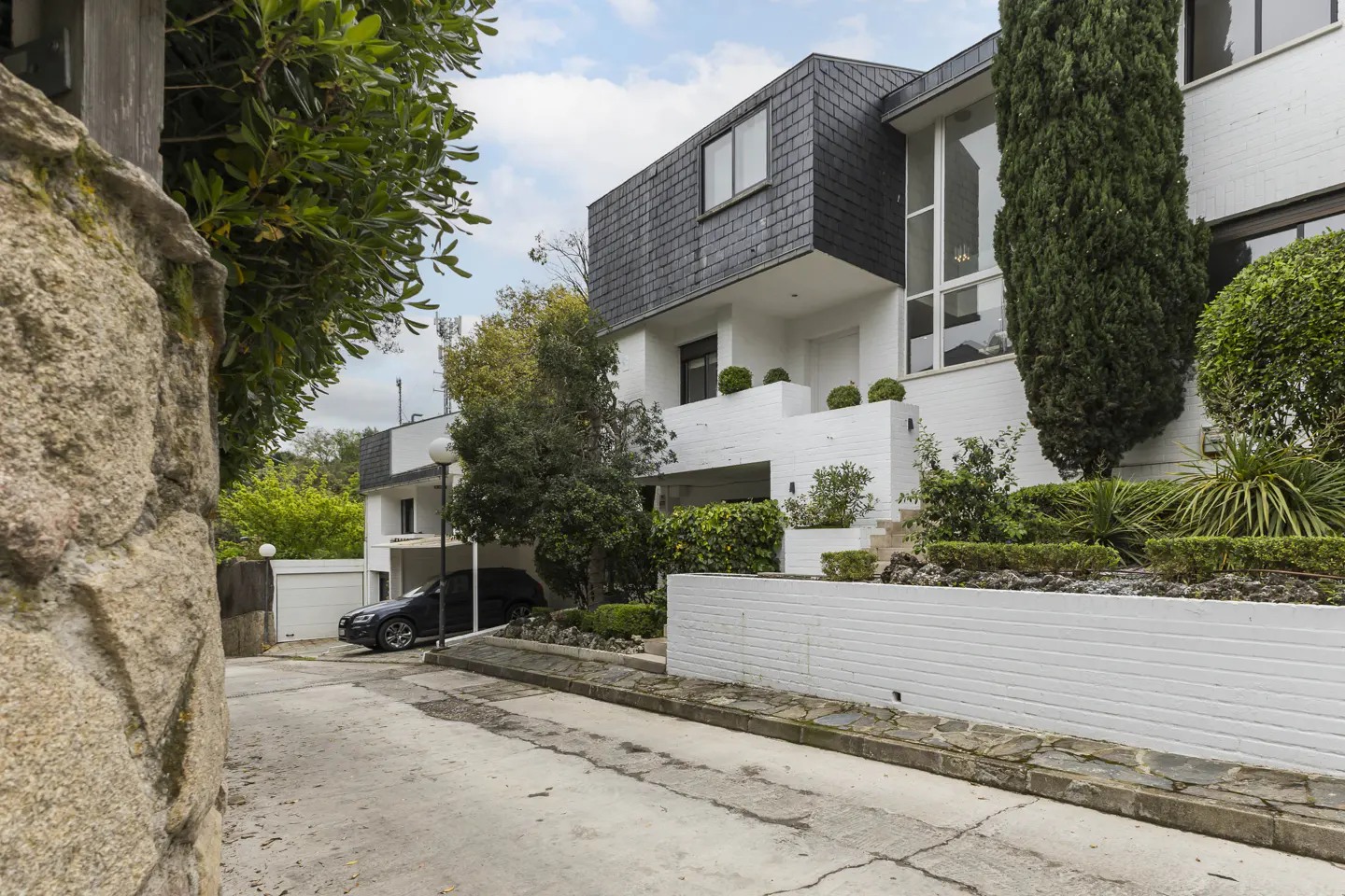 Exterior view of a modern white house with a dark gray roof and a car parked in the driveway.