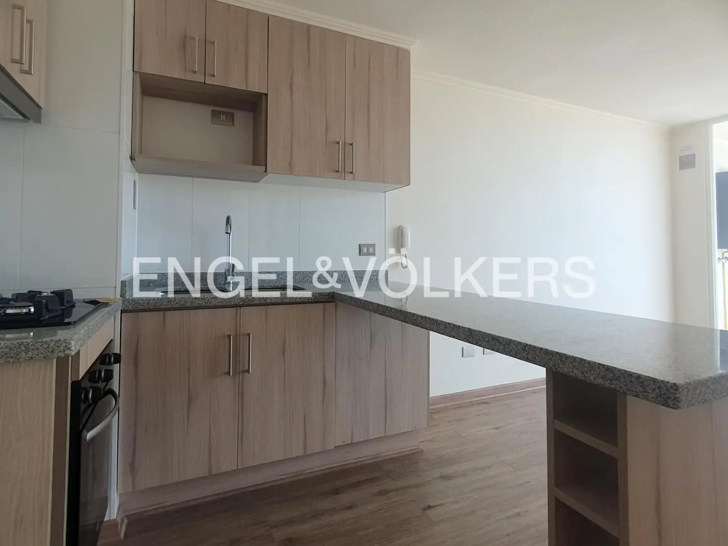A kitchen with light wood cabinets, granite countertops, and a breakfast bar. The floor is light wood. White walls.