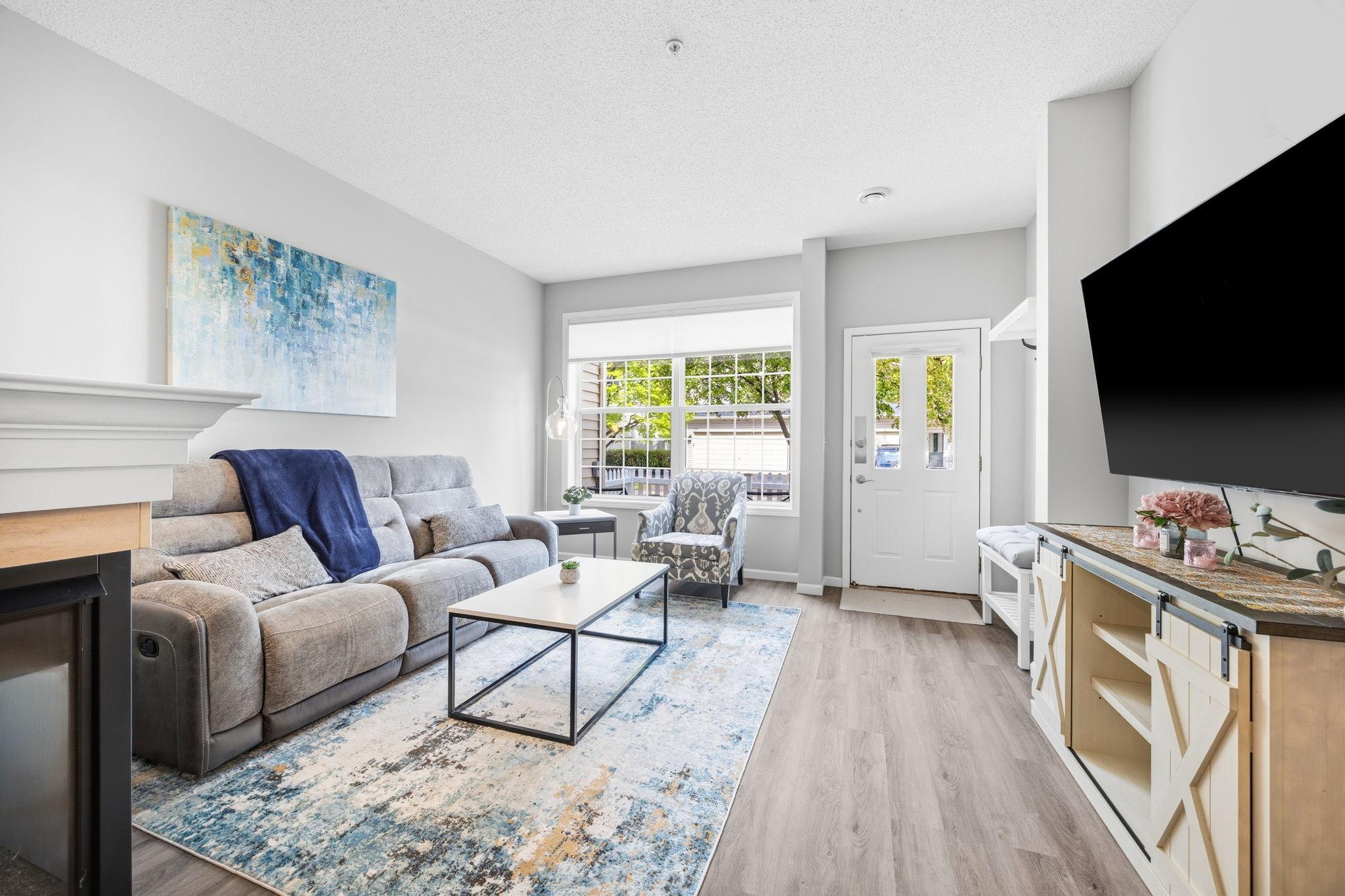 Bright living room with gray sofa, blue accents, and a white door. A large TV sits on a rustic cabinet.