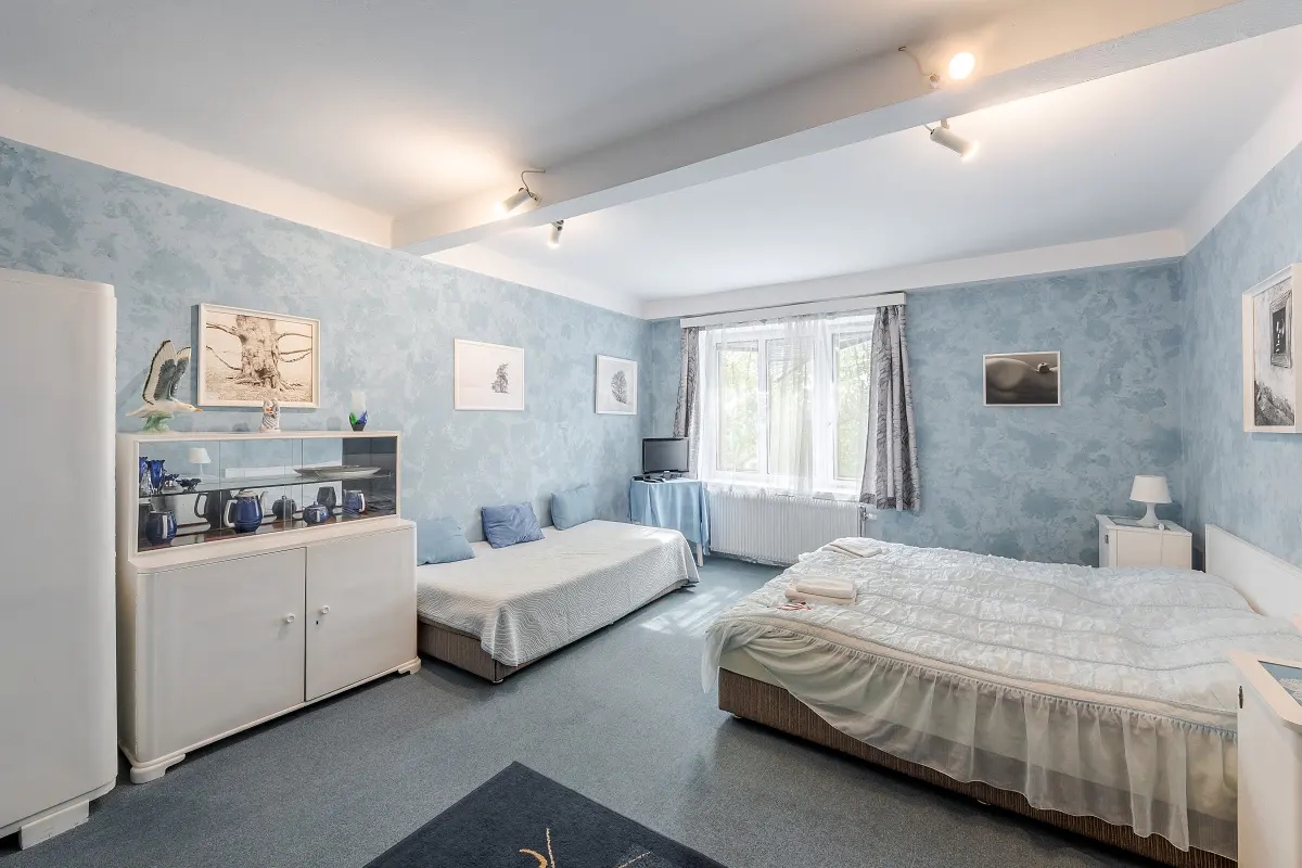 A light blue bedroom with two beds, a white wardrobe, and blue accents. Artwork hangs on the textured walls.