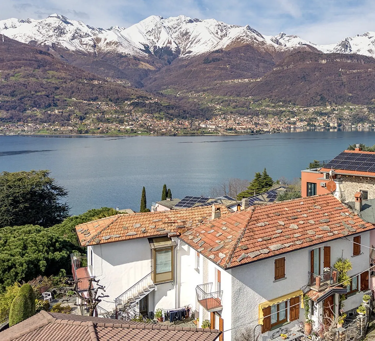 Scenic view of white houses with red tile roofs overlooking a blue lake and snow-capped mountains.