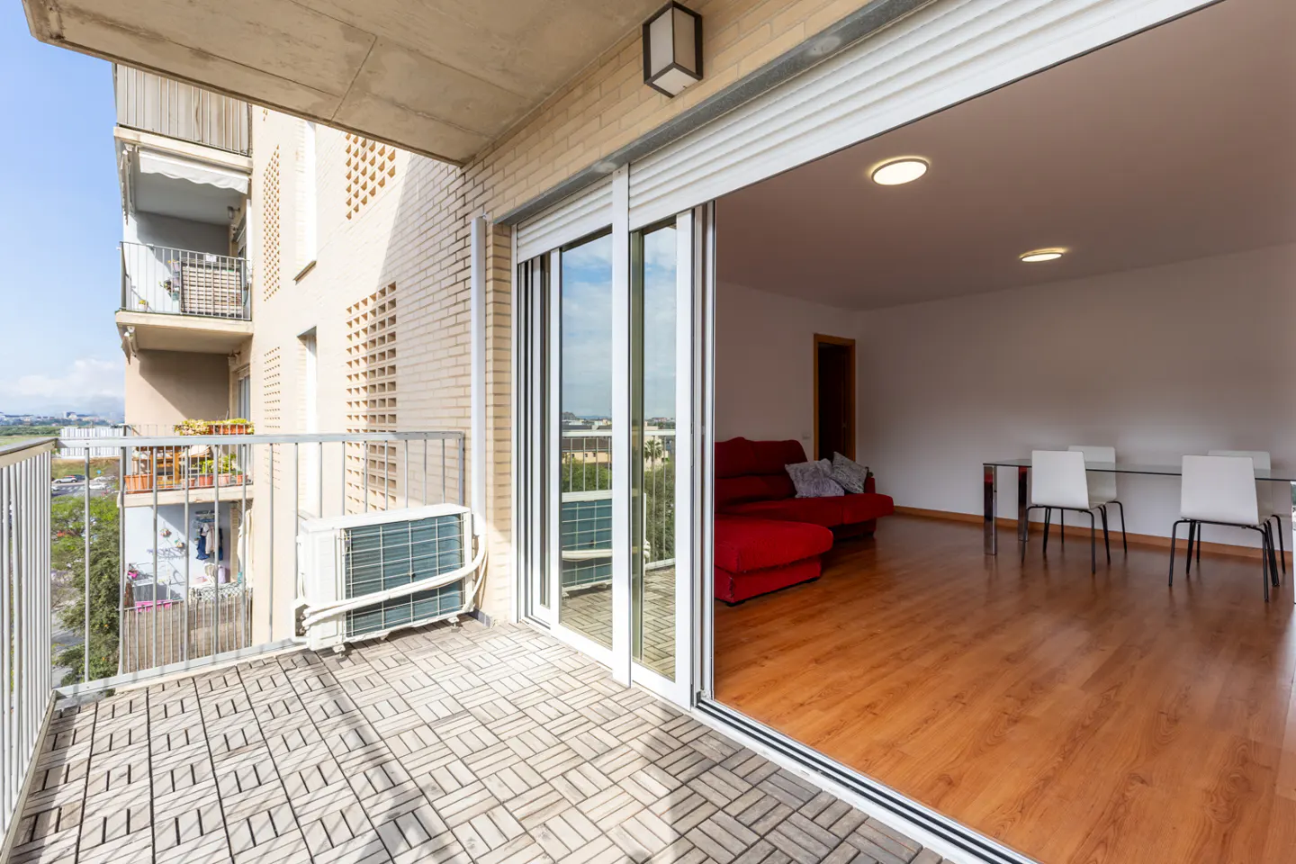 Balcony with sliding glass doors open to a living room with a red sofa and dining table.