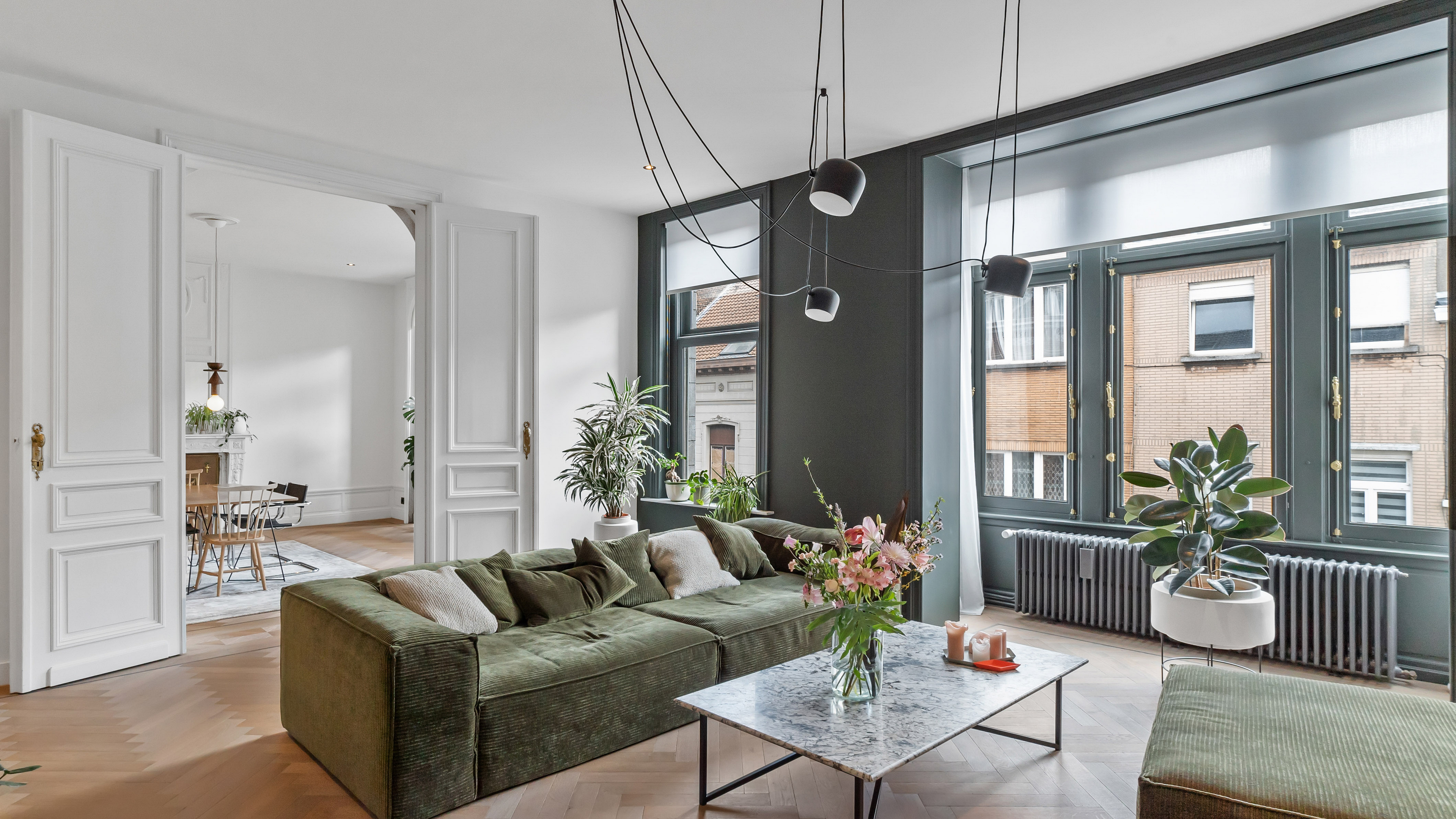 Modern living room with a green velvet sofa, marble coffee table, and large windows overlooking a city street. [AI-generated text]