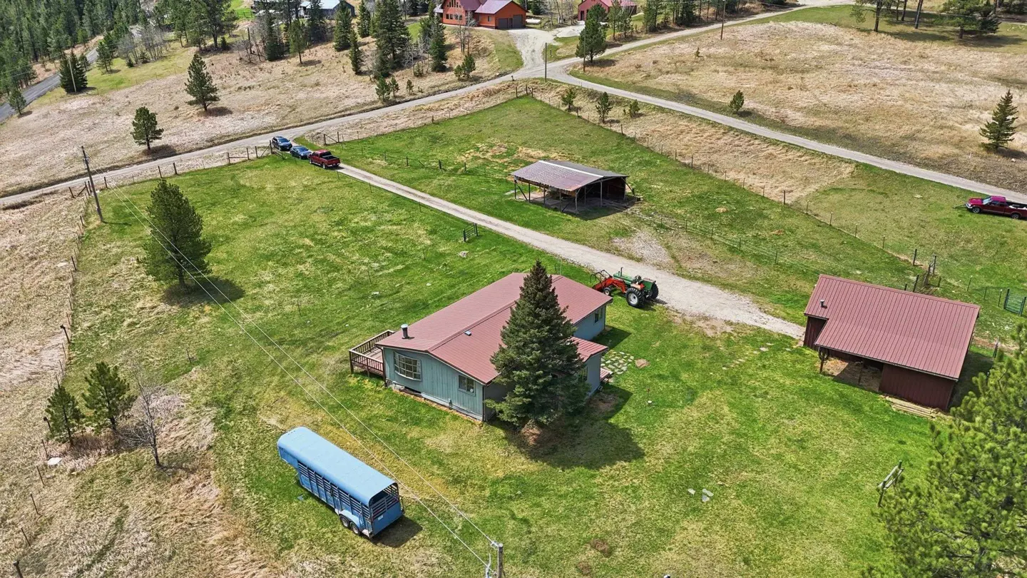 Aerial view of a rural property with a house, two outbuildings, a tractor, and a horse trailer on a grassy lot.