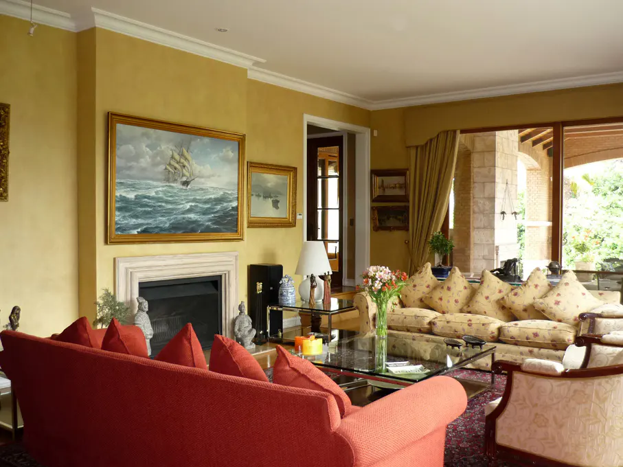 Living room with yellow walls, a red sofa, and a floral sofa. A painting of a ship hangs above the fireplace.