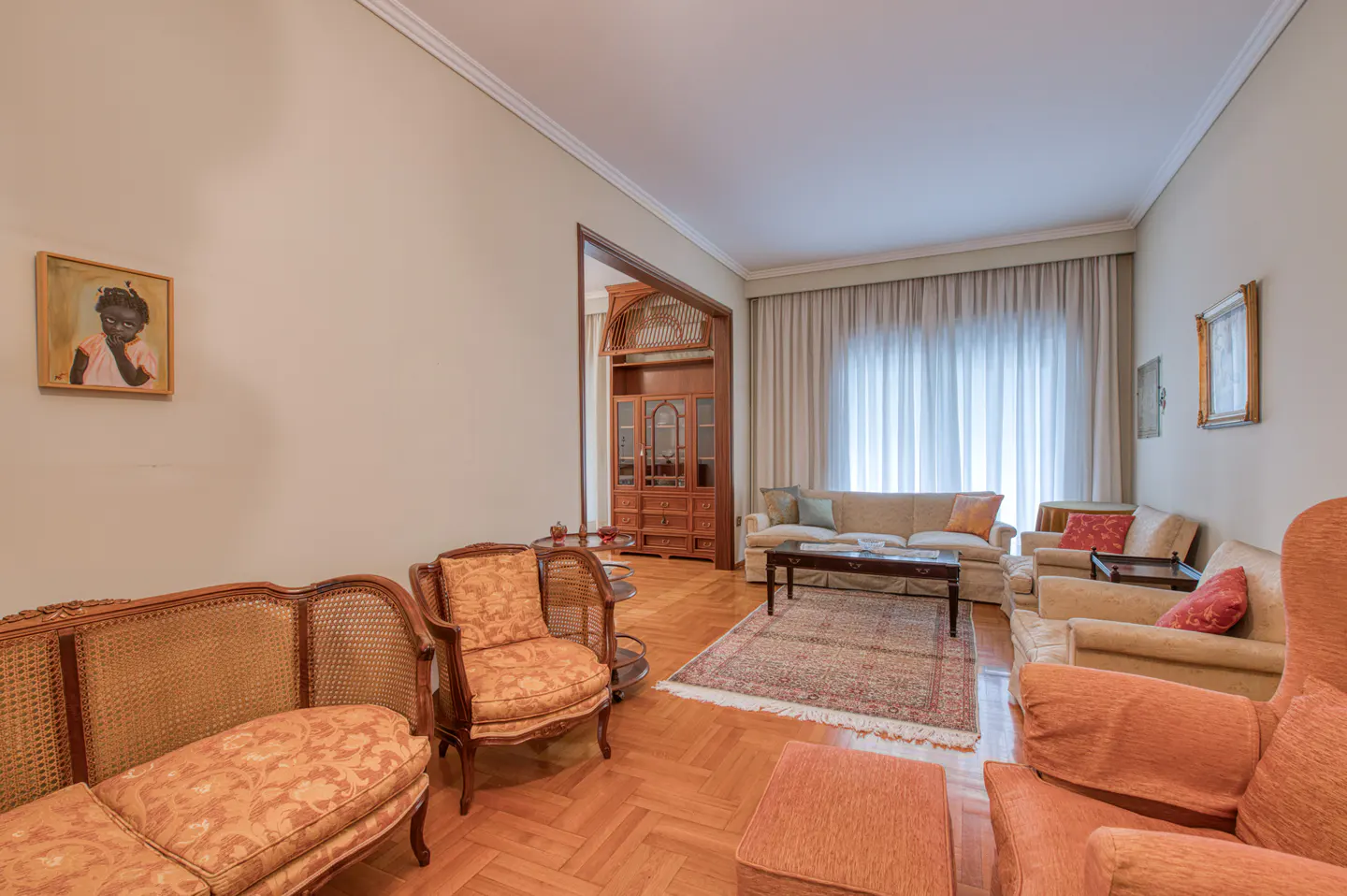 Living room with beige walls, hardwood floors, sofas, chairs, a rug, and a painting of a child on the wall.