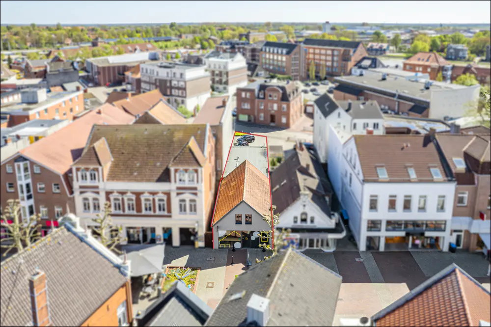 Aerial view of a narrow building with a red-tiled roof in a dense town center, highlighted by a red outline.