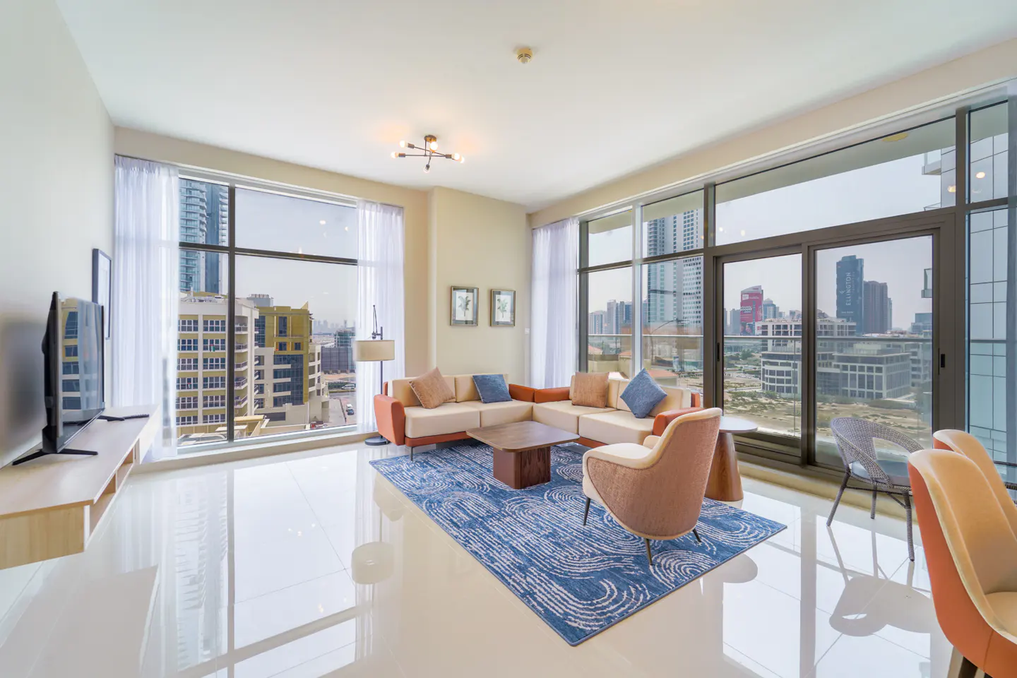Bright living room with a beige sectional sofa, blue rug, and city views from large windows.