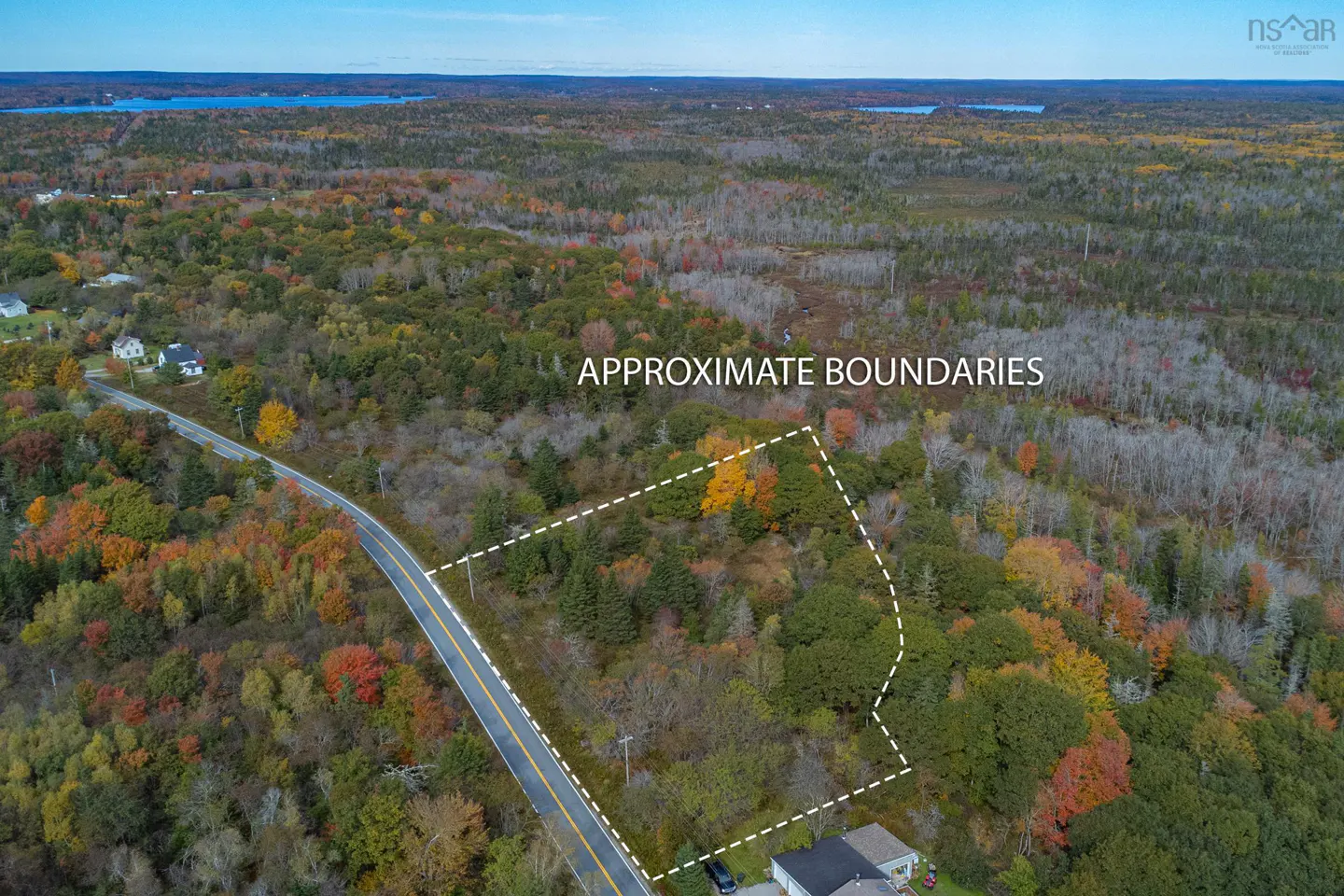 Aerial view of a wooded lot with approximate boundaries marked in white, next to a road in autumn.
